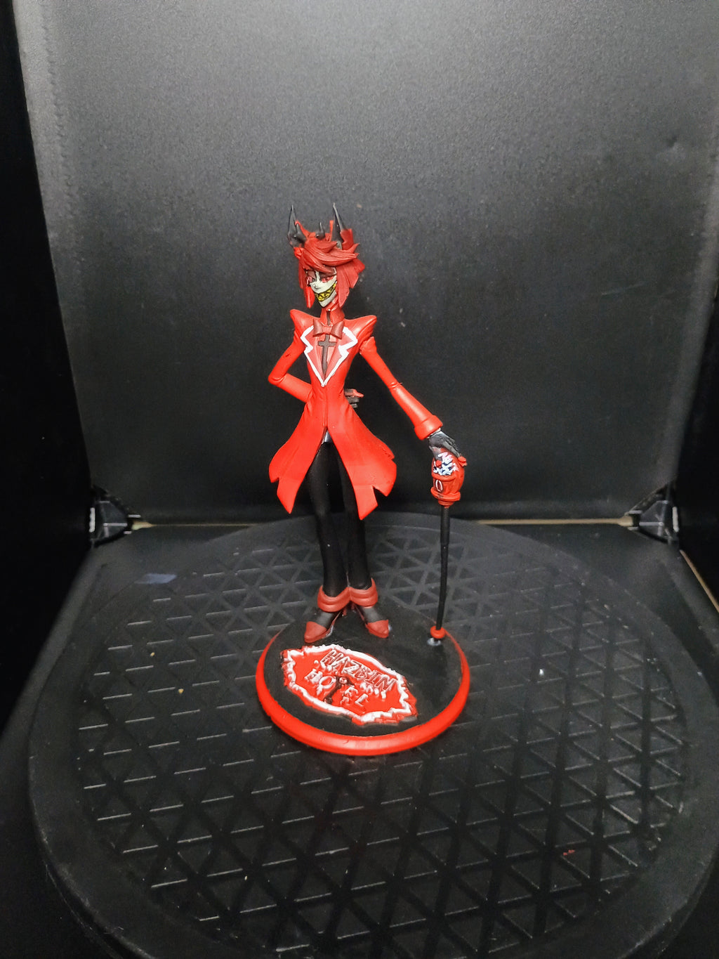 A red and black anime-style figurine of a horned character standing on a circular base, photographed against a dark backdrop.